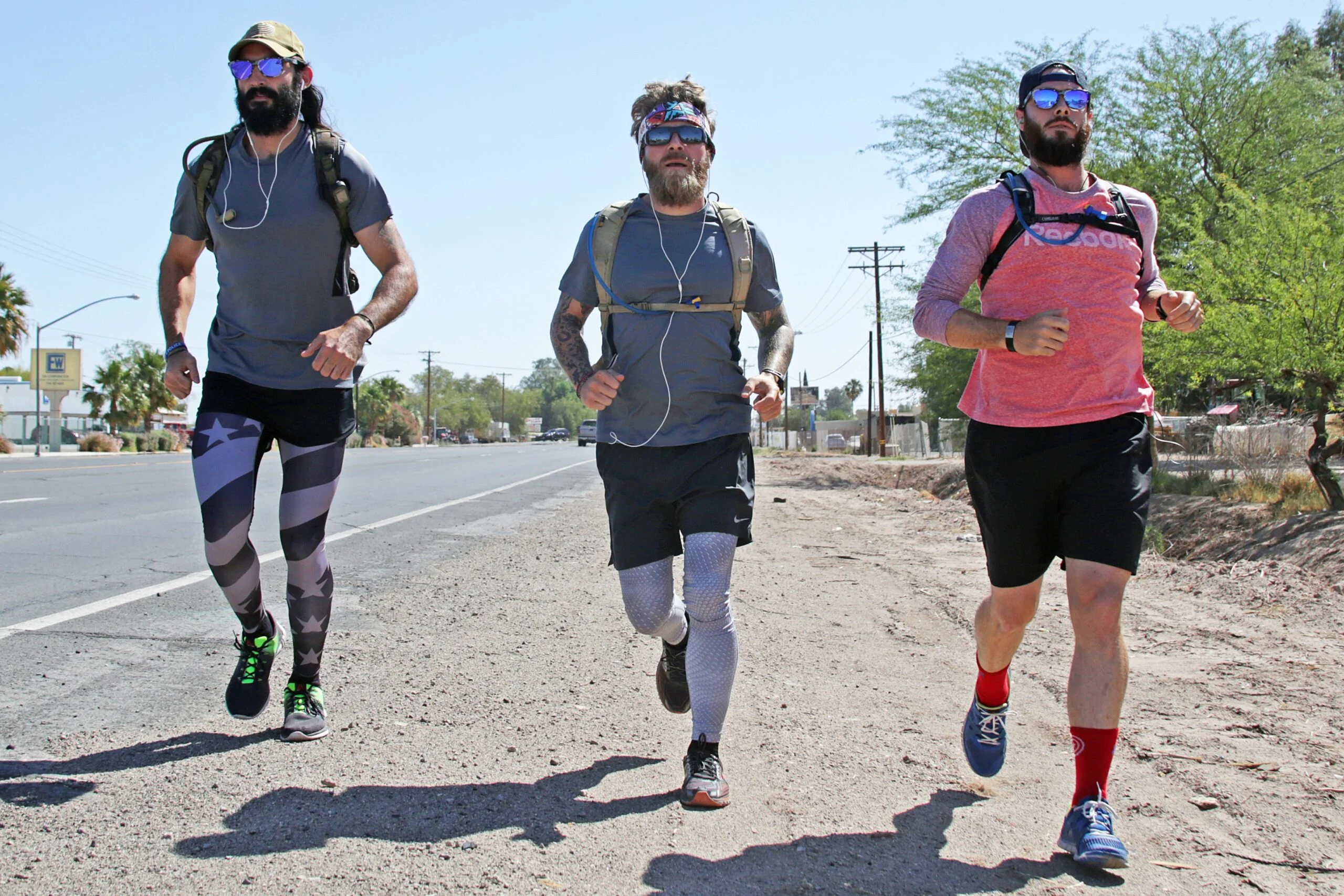 Three bearded runners with hydration packs running along a desert highway